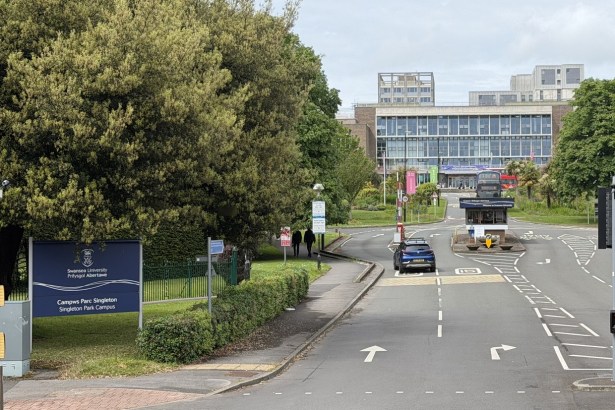The entrance road to Swansea University's Singleton Park campus, with the blue bilingual university sign on the left and the main building at the end of the drive