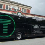 A black TaithCymru coach with a large green T logo parked outside Bangor railway station, the route's stops from Bangor to Carmarthen listed along its side