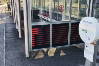 A white circular Transport for Wales help point unit mounted beside a station shelter on a platform