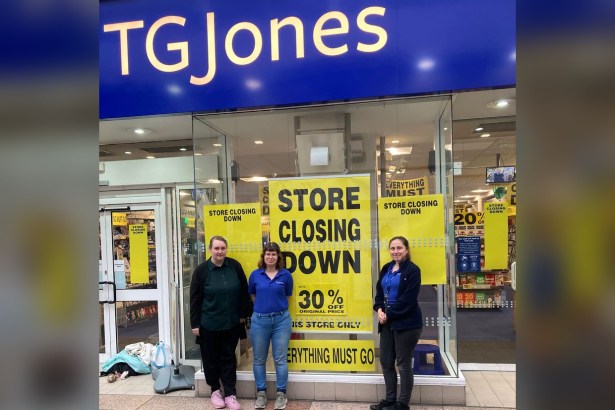 Three shop staff standing in front of the TGJones store in Bridgend's Rhiw Shopping Centre, with yellow 'store closing down, up to 30% off' posters filling the window behind them