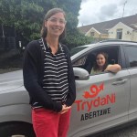 A woman standing beside a grey Hyundai Kona in TrydaNi Abertawe livery, with another woman at the wheel