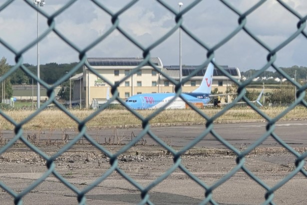 A TUI aircraft on the tarmac at Cardiff Airport seen through the perimeter fence, with the airport's Holiday Inn Express behind