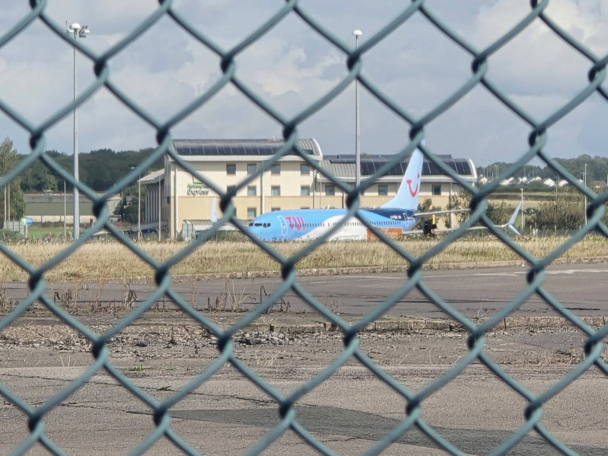 A TUI aircraft on the tarmac at Cardiff Airport seen through the perimeter fence, with the airport's Holiday Inn Express behind