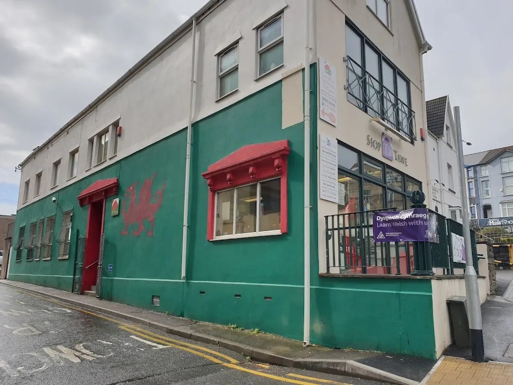 The green and cream frontage of Tŷ Tawe on Christina Street, Swansea, with a red dragon painted on the wall and a Learn Welsh banner on the railings