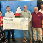 Five people standing in front of an Urdd banner holding a large Persimmon cheque made out to Urdd Gobaith Cymru for £2,500