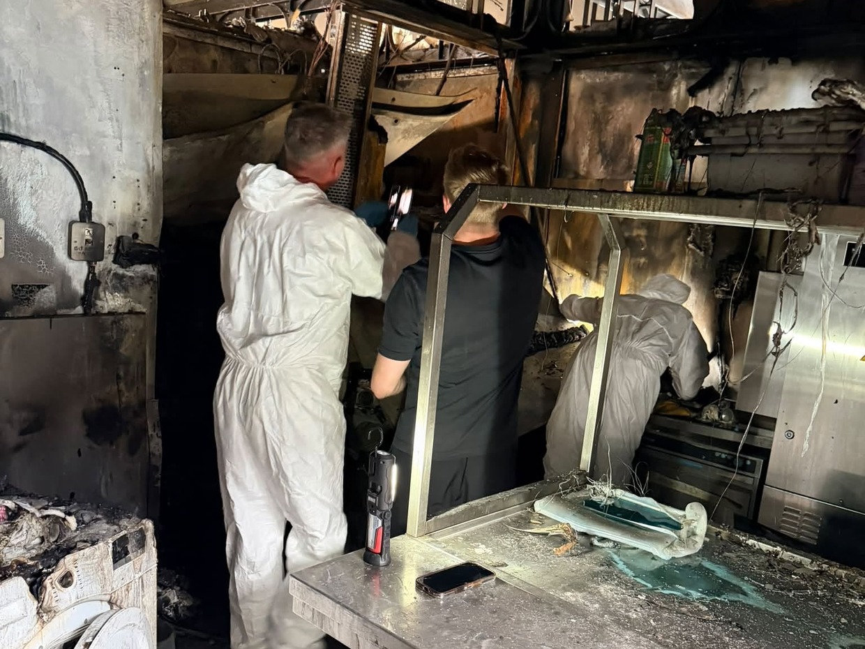 People in white protective suits examining the burnt-out kitchen at Verdi's in Mumbles, with scorched walls, ceiling and steel counters