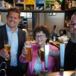 First Minister Rhun ap Iorwerth, Finance Minister Elin Jones and pub owner Phil Newbould raising glasses behind the bar at the Radyr Tap