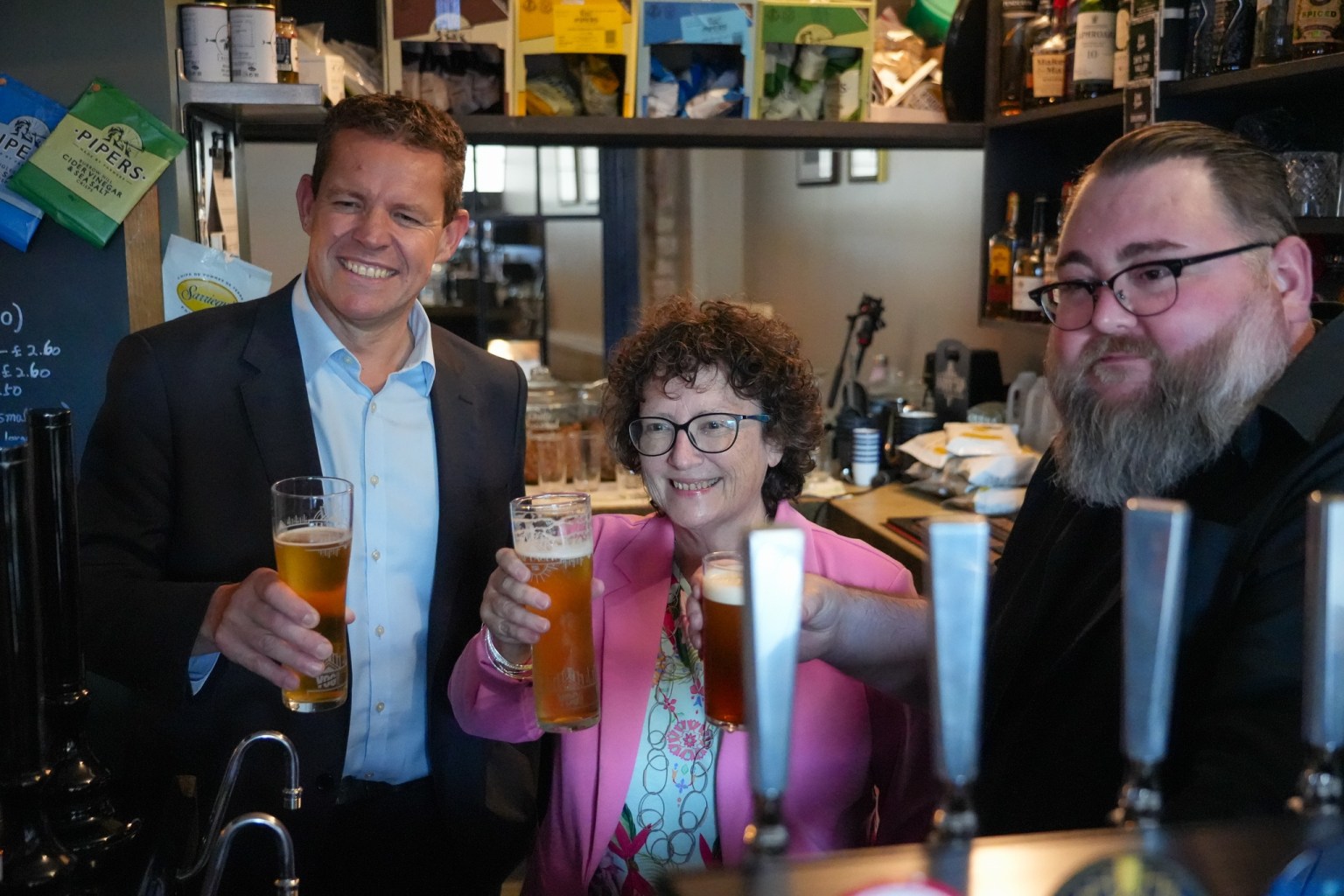 First Minister Rhun ap Iorwerth, Finance Minister Elin Jones and pub owner Phil Newbould raising glasses behind the bar at the Radyr Tap
