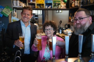 First Minister Rhun ap Iorwerth, Finance Minister Elin Jones and pub owner Phil Newbould raising glasses behind the bar at the Radyr Tap