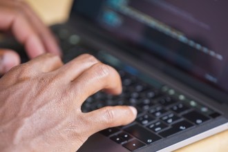 Hands typing on a laptop keyboard, illustrating a Welsh Government partnership on Welsh language AI