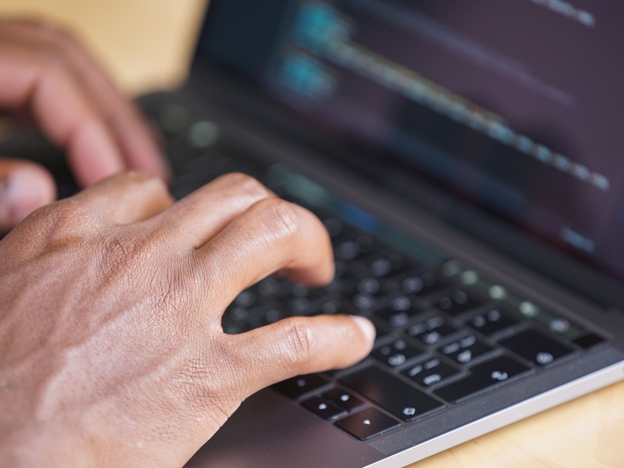 Hands typing on a laptop keyboard, illustrating a Welsh Government partnership on Welsh language AI