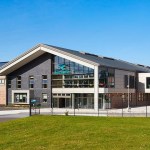 The modern brick and slate front of Ysgol Bro Dinefwr in Llandeilo under a blue sky, with solar panels on the roof and pupils crossing the grounds