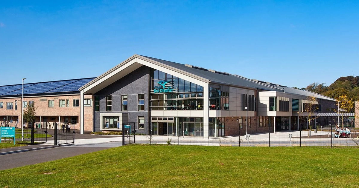 The modern brick and slate front of Ysgol Bro Dinefwr in Llandeilo under a blue sky, with solar panels on the roof and pupils crossing the grounds