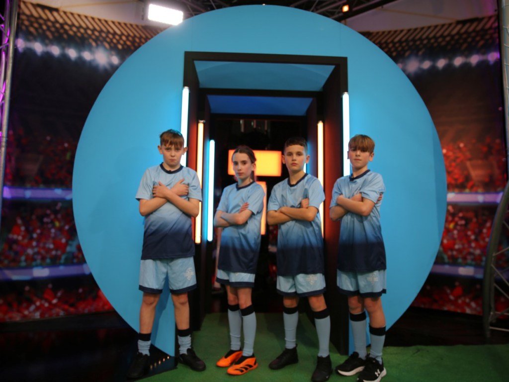 Four Ysgol Lôn Las pupils in blue Tekkers kit standing with arms crossed in front of the show's blue circle set
