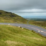 The A4069 Black Mountain road winding across open hillside in Carmarthenshire, with sheep on the verge and the carriageway and farmland stretching into the distance