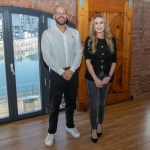 Alix Charles and James Smale-Davies standing in an empty brick-walled office unit at the J-Shed, with the dock visible through arched windows