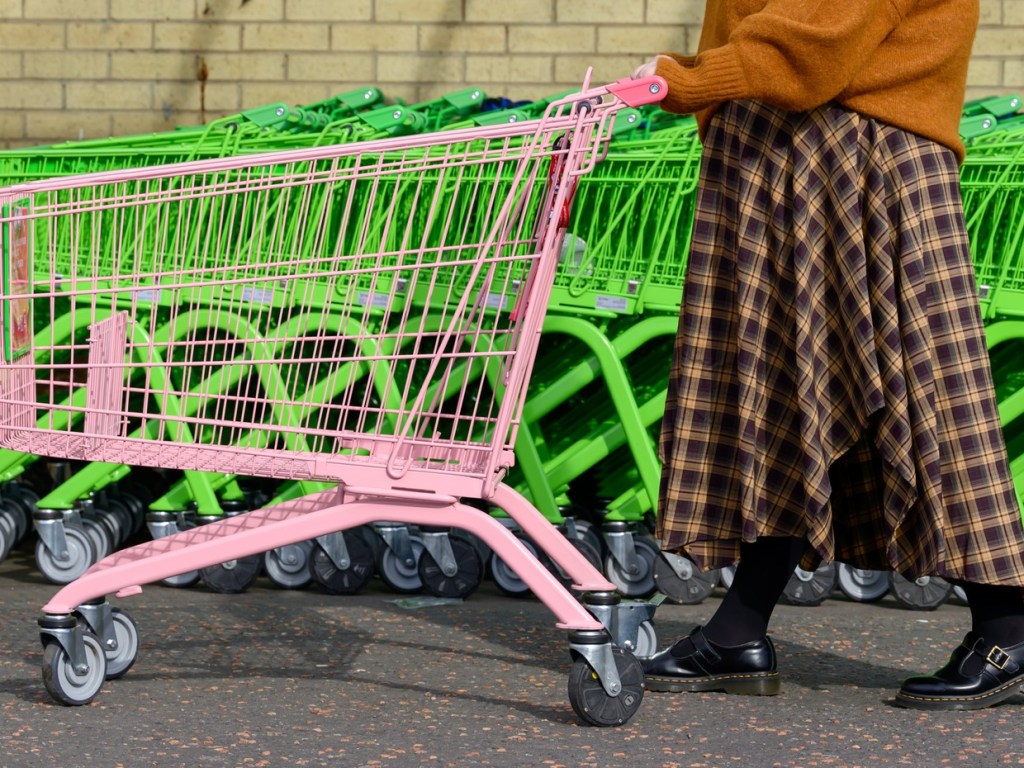 A single pink shopping trolley being pushed past a long row of green Asda trolleys outside a store