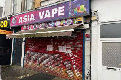 The red graffiti-covered shutter of Asia Vape on St Helen's Road, Swansea, with court closure notices taped to it under the shop's purple and pink sign