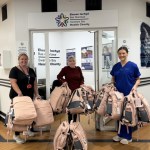 Maria Bailey and two others holding armfuls of pink Bailey's Bags backpacks outside the Swansea Bay Health Charity office