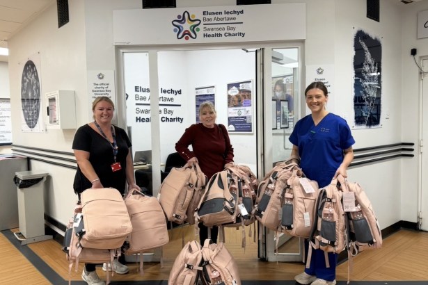 Maria Bailey and two others holding armfuls of pink Bailey's Bags backpacks outside the Swansea Bay Health Charity office