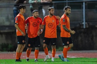 Bradley Gibbings, second from right, celebrating with three Pure Swansea team-mates in orange shirts on the pitch at night