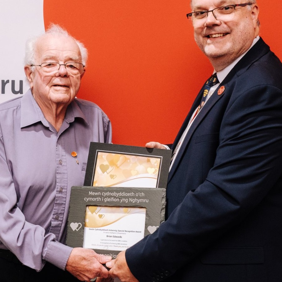 Close-up of Brian Edwards holding his slate special recognition award with Peter Richardson of the Welsh Blood Service