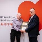Brian Edwards, 83, holding a slate award with Peter Richardson of the Welsh Blood Service in front of a red heart backdrop