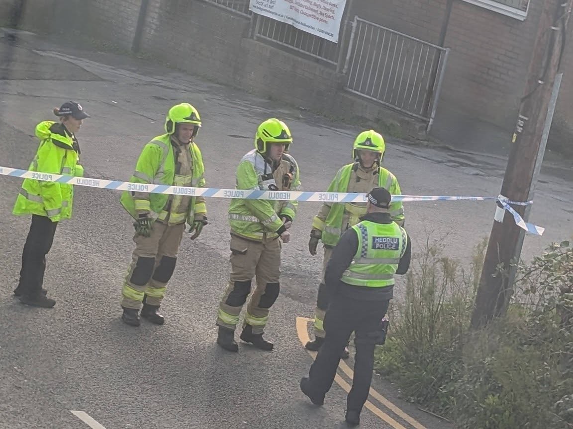 Three firefighters in helmets and two police officers at a police tape cordon across a road in Bridgend
