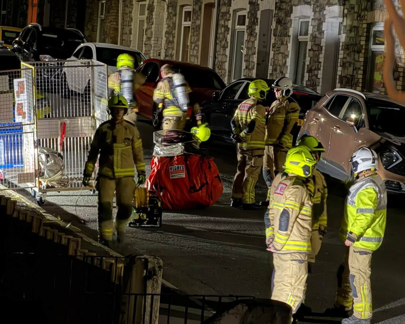 Firefighters, some wearing breathing apparatus, with equipment laid out in a terraced street at night