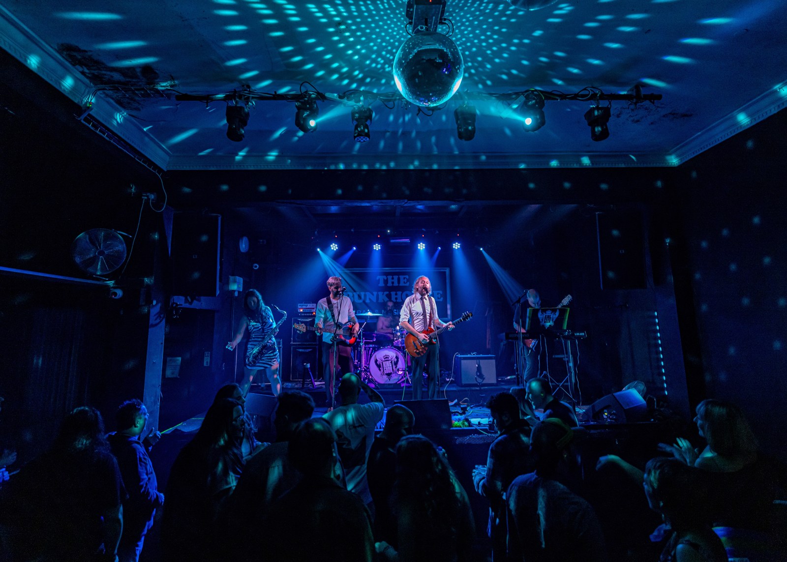 A band on stage at The Bunkhouse under a mirror ball and blue lights with a crowd watching