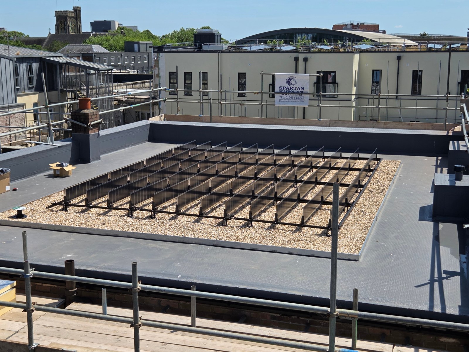 Rows of vertical solar panels on a bed of crushed shells on the new flat roof of The Bunkhouse, with Swansea rooftops behind