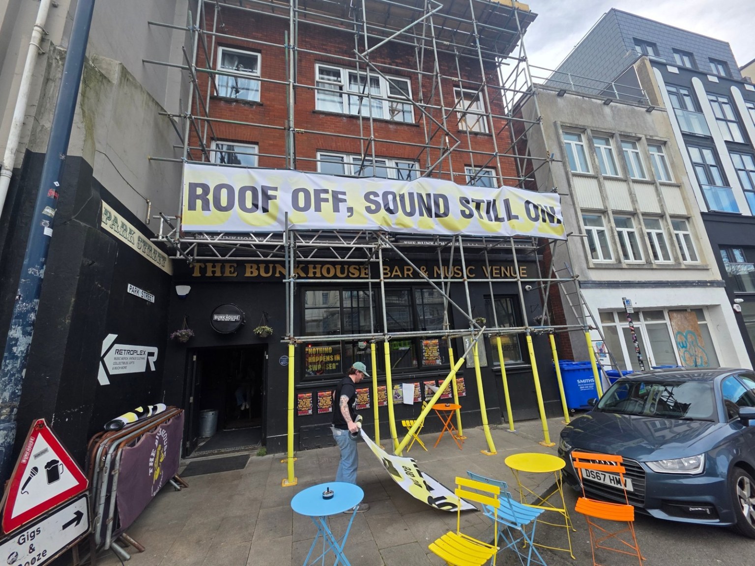 A banner reading Roof off, sound still on hung on scaffolding over the black frontage of The Bunkhouse bar and music venue on the Kingsway, Swansea