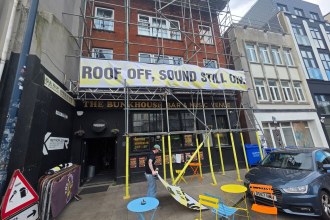 A banner reading Roof off, sound still on hung on scaffolding over the black frontage of The Bunkhouse bar and music venue on the Kingsway, Swansea
