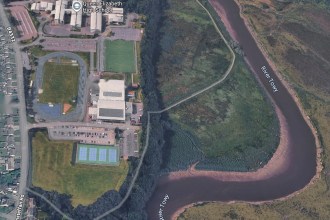 Aerial view of Carmarthen Leisure Centre in Johnstown with the grassed field beside its tennis courts, Llansteffan Road to the left and the River Towy to the right