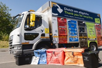 A Carmarthenshire Council recycling lorry with coloured compartments, parked behind blue, red and orange reusable sacks, a white battery sack and black food caddies