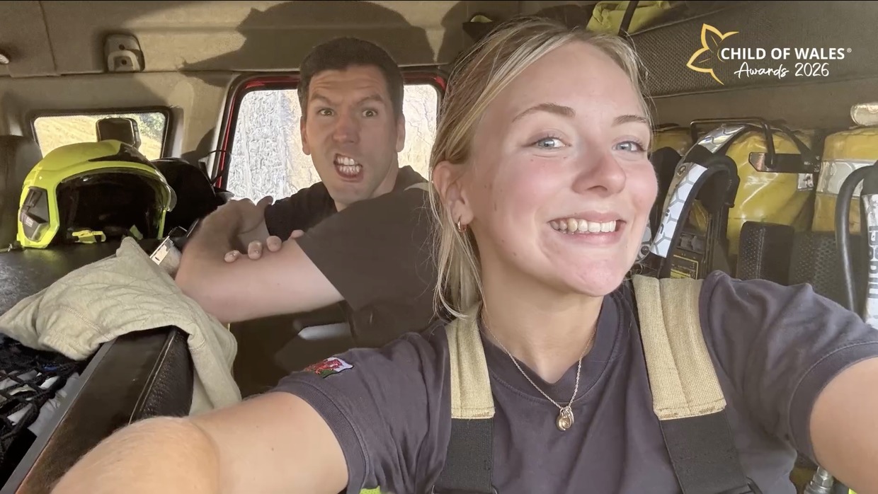 Cathryn Moore smiling in a selfie taken in the cab of a fire engine, with a fellow firefighter pulling a face behind her
