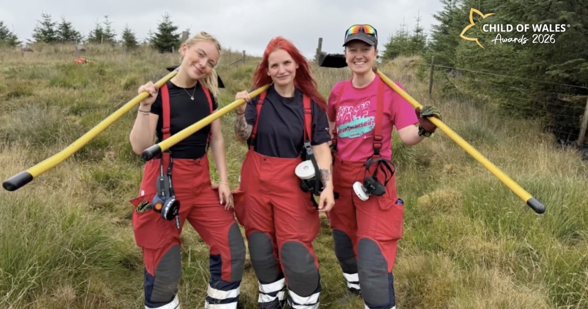 Three female firefighters in red fire trousers standing on moorland with yellow fire beaters over their shoulders, Cathryn Moore on the left