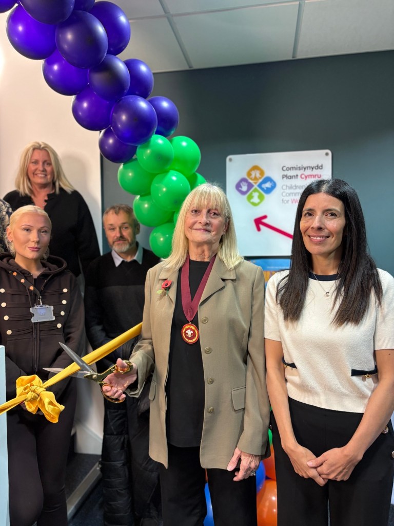 Susan A Jones, Deputy Lieutenant of West Glamorgan, holding ribbon-cutting scissors beside Children’s Commissioner Rocio Cifuentes under purple and green balloons