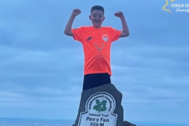 Cian Evans, 11, in an orange top, raising both arms at the National Trust Pen y Fan 886m summit marker