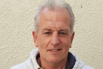 Head-and-shoulders photo of Clifford Foster, a grey-haired man in a white hooded top, against a cream wall