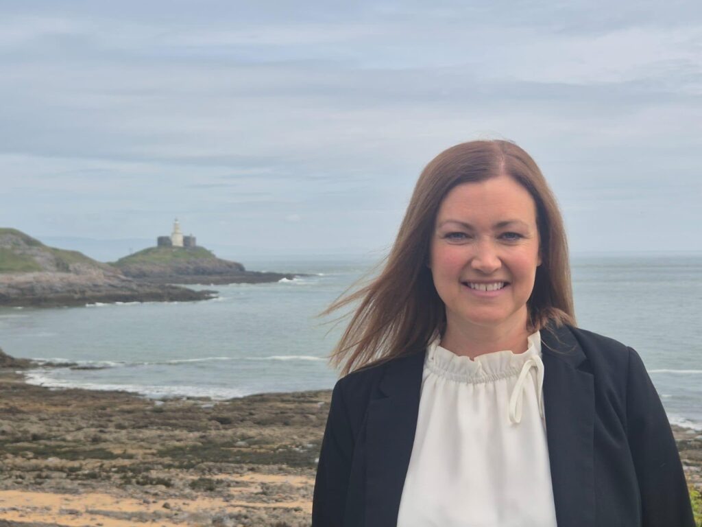 Cllr Hannah Williams smiling on the coast at Mumbles, with the lighthouse on Mumbles Head behind her