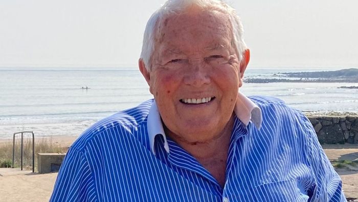Cllr Richard Lewis in a blue striped shirt smiling on the seafront with the beach and sea behind him
