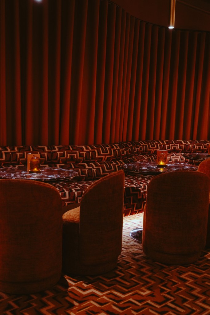 Curved velvet booth seating around small tables under heavy red curtains in a dimly lit Cosy Club
