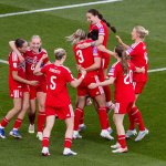 Cymru Women players in red kits hugging and celebrating together on the pitch