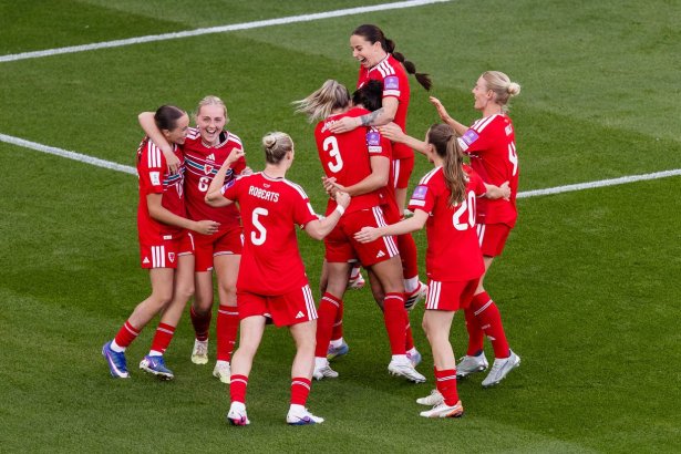 Cymru Women players in red kits hugging and celebrating together on the pitch