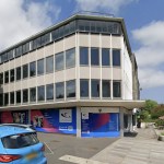The former TSB bank on the corner of the Kingsway and Craddock Street in Swansea, a three-storey 1960s office block with its ground floor boarded up behind Gower College Swansea advertising hoardings