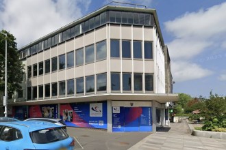The former TSB bank on the corner of the Kingsway and Craddock Street in Swansea, a three-storey 1960s office block with its ground floor boarded up behind Gower College Swansea advertising hoardings