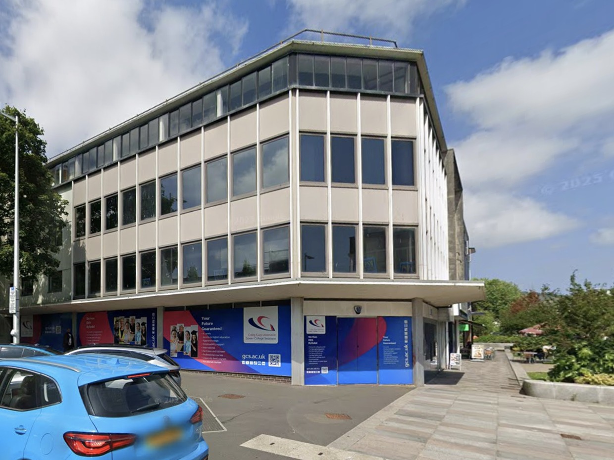 The former TSB bank on the corner of the Kingsway and Craddock Street in Swansea, a three-storey 1960s office block with its ground floor boarded up behind Gower College Swansea advertising hoardings