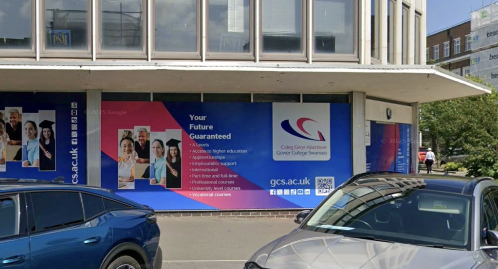 Close-up of the boarded-up ground floor of the former TSB bank on the Kingsway in Swansea, covered in Gower College Swansea branded hoardings