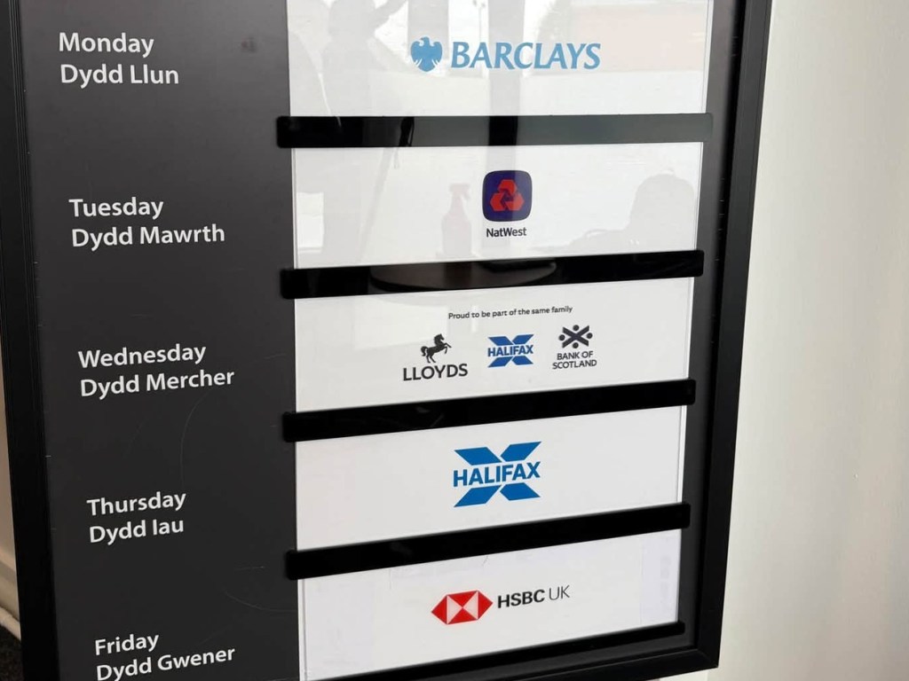 Bilingual rota board inside the Gorseinon banking hub showing Barclays on Monday, NatWest on Tuesday, Lloyds, Halifax and Bank of Scotland on Wednesday, Halifax on Thursday and HSBC UK on Friday